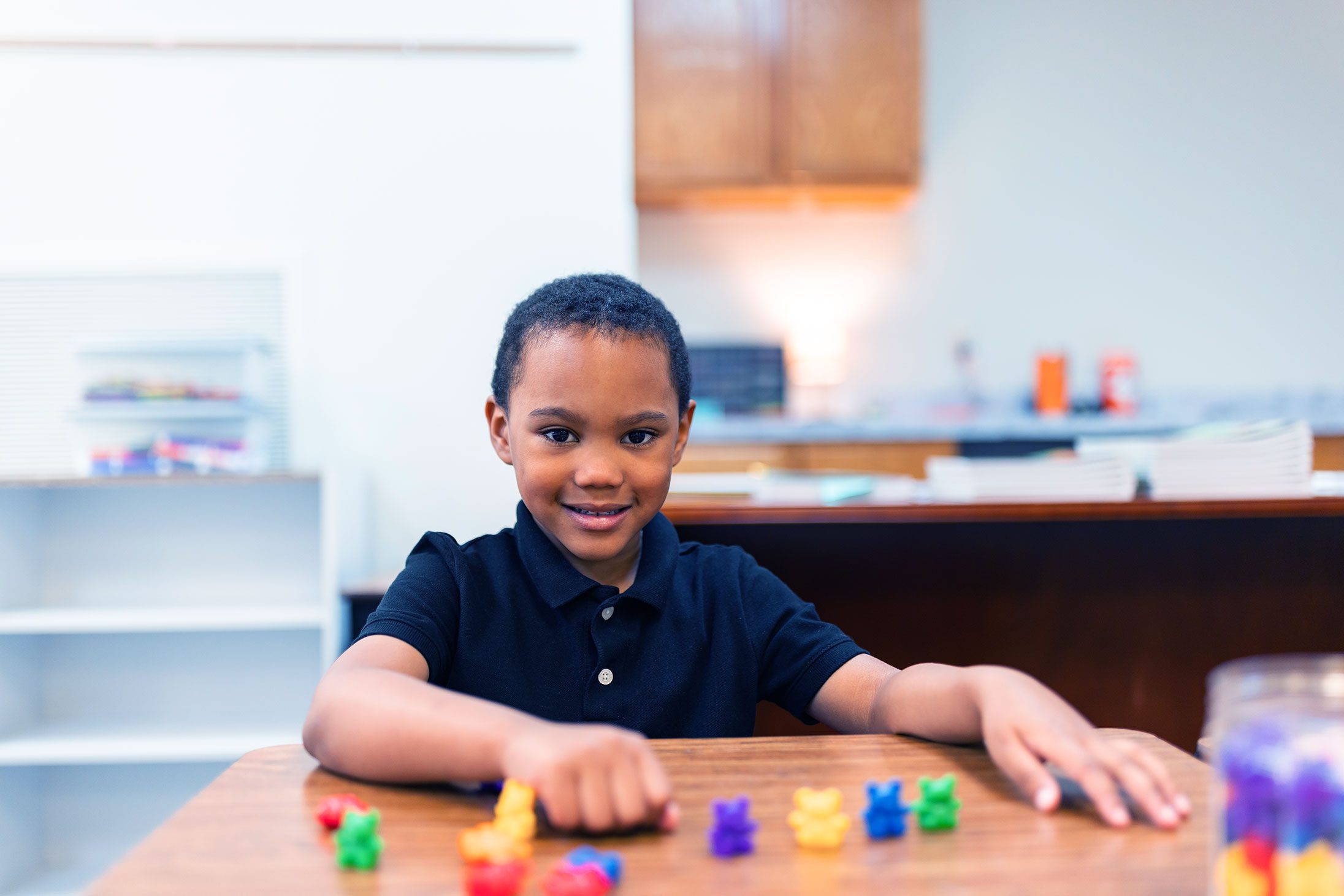 Smiling student at a desk with colorful counting bears.