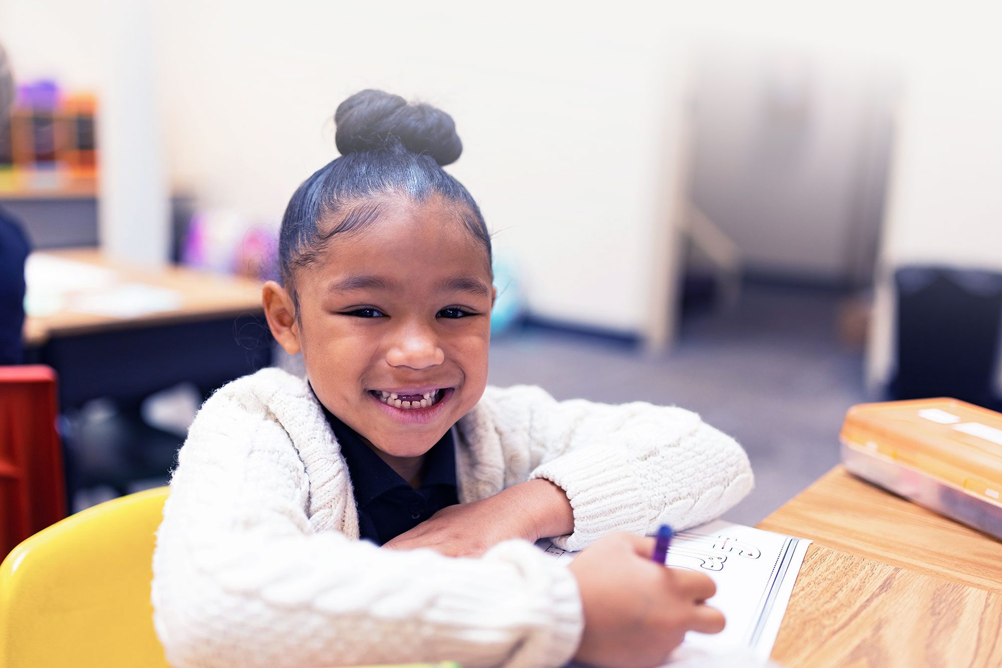 Smiling student doing a writing assignment in a classroom.